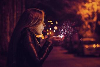 Woman blowing into her palm. Sparkles of light ascend into the air.